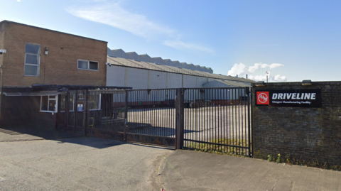 The entrance to the Albion Automotive plant in Scotstoun in Glasgow - there is a sign on a wall, with gates leading into the plant next to it.