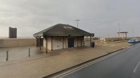 Google streetview of kiosk on beach promenade with cars parked on road next to it.