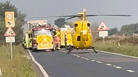 Helicopter on a road, surrounded by emergency vehicles.
