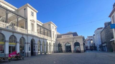 Market Square, St Peter Port, Guernsey. A large white former market building with a cobbled square in front.