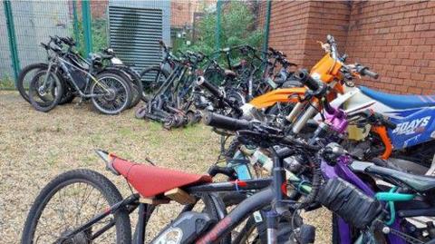 Rows of 40 seized bikes are seen lined around a yard next to a redbrick building.