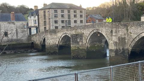 Dau berson mewn siacedi llachar yn sefyll ar bont dros Afon Teifi yn Aberteifi ble mae ofnau bod dyn wedi mynd i'r afon