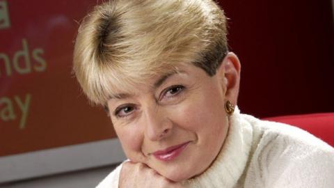 Former ý news presenter Kay Alexander looks at the camera wearing a white polo neck sweater with her chin resting on her hand