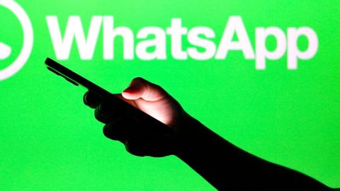 A person holds a phone up near a WhatsApp symbol background