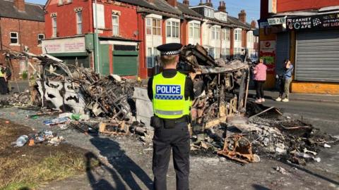 Police patrol a burned out bus in Harehills 