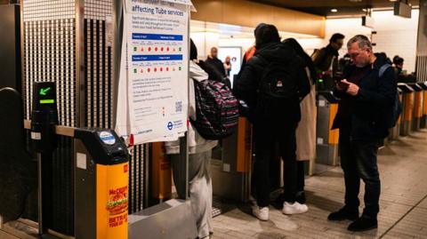 People at the barrier gates at a Tube station beside a sign warning about strike action