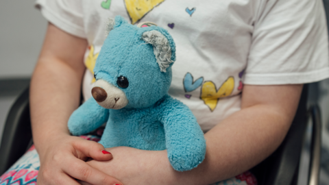 A pair of childs arms, with painted nails cuddling a blue teddy