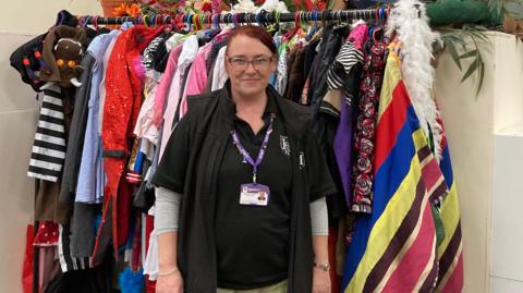 Eleanor 'Elle' Dicks, founder of Haddon Charity of Performing Arts, standing in front of a multi-coloured costume rack. 