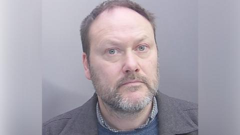 A headshot of a man in his late 40s with a beard looking directly into the camera