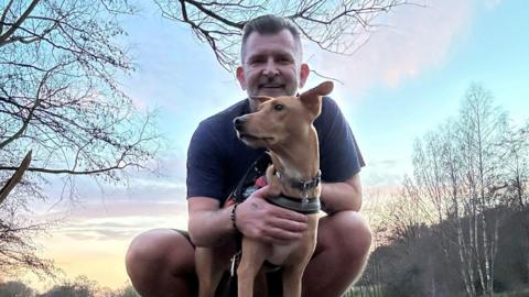 Shawn Leek wearing shorts and a T-shirt while with a dog