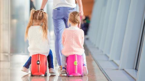 Two young girls sitting on Trunkis, kids' suitcases on wheels in an airport. 