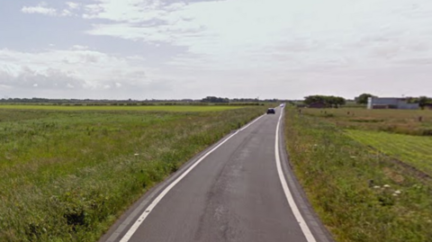 A car drives along an empty Lytham St Annes Way with fields on either side