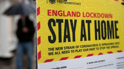 A government sign warning people to stay at home on a street in Winchester. It is covered in rain droplets.