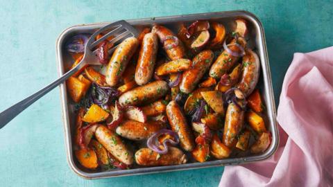 An over tray filled with apple, sausage and vegetables. 