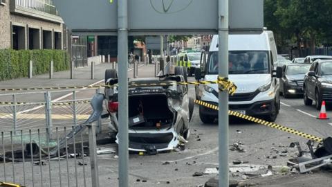 An overturned car at a city road junction, with cars and debris nearby