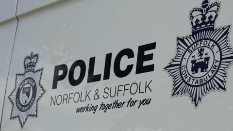 A close up of a white police van's logo that reads: Police, Norfolk & Suffolk, working together for you. Both police force's logos sit on each side of the writing.