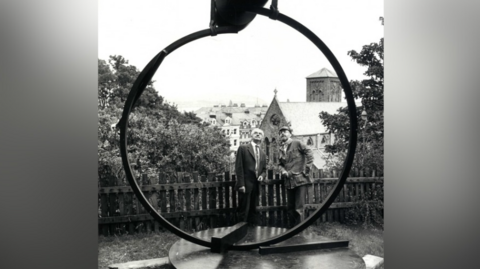 Yn Arreyder is a large steel ring twisted to hold aloft a heavy double dome, positioned to look out across Douglas Bay towards the sunrise.