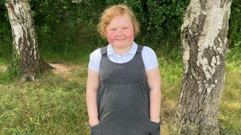 A young girl with ginger hair stood smiling 