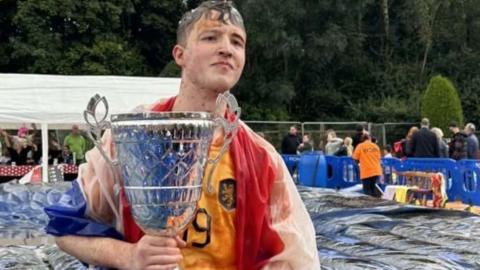 George Young, the winner of the World Gravy Wrestling Championships,  at the Rose 'N, Bowl pub holds a trophy with a gravy-soaked face and draped in a gravy-stained flag