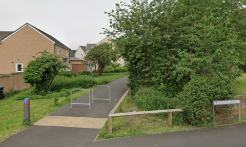 The image shows the start of an alleyway running through a green space and past a housing estate.