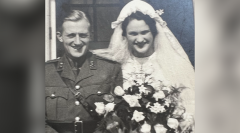 An old black and white photo dating back to the 1940s of Rex and Margaret at their wedding. Rex is dressed in military uniform and Margaret is wearing a white dress and veil. She is holding a bouquet of flowers. Both of them are looking at the camera and smiling.
