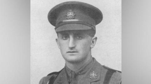 A black and white image of Nowell Oxland. He is wearing a military uniform, including a hat. He has a serious expression and is looking at the camera.