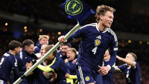 Scott McTominay runs off with a corner flag while his teammates celebrate behind him