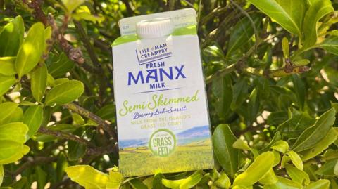 A pint of Manx milk with green labelling rests in front of a green bush.