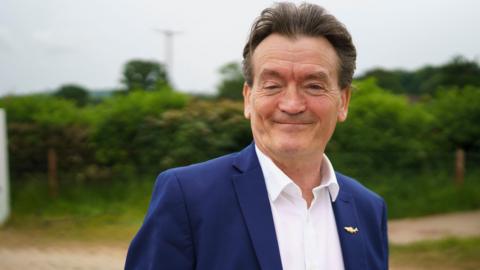 Feargal Sharkey looking at the camera and smiling, he is wearing a blue suit and white shirt.