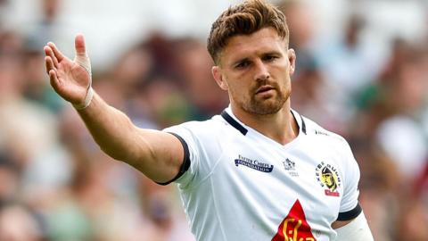 Henry Slade in a white shirt holds his hand out to the right