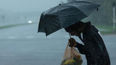 A man holding a black umbrella in the rain hunches over as he crosses a deserted road in Orlando, Florida 