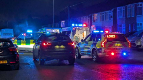 The scene of a crash in Wherstead Road, Ipswich. A police car and two ambulances can be seen, with blue lights on. It is dark and there are terraced houses towards the righthand side.