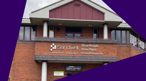 A redbrick two-storey building with a triangular roof. The building has windows all along the top floor, which have maroon window frames. The building says "Sandwell" in large white letters on the front.