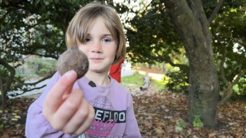 Celestine pictured in a purple sweatshirt pictured standing holding a conker up to the camera.
