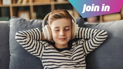 A boy in a navy and cream striped top has his hands behind his head as he relaxes on the sofa. He wears a pair of headphones and has a calm smile on his face