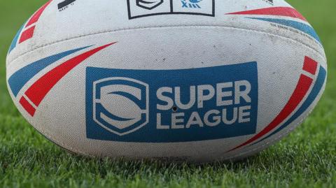 A rugby league ball, displaying the Super League logo, sits on the grass