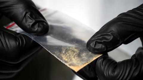 Hands wearing back gloves hold nitazene powder
