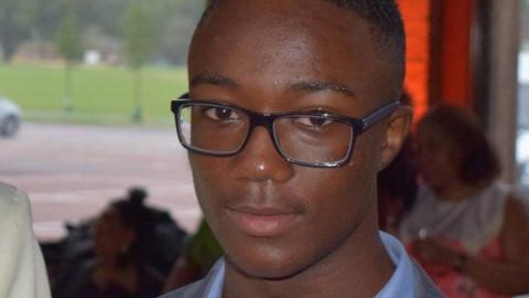 Jamel Boyce, a 17-year-old wearing glasses and a suit, looks at the camera at a social event