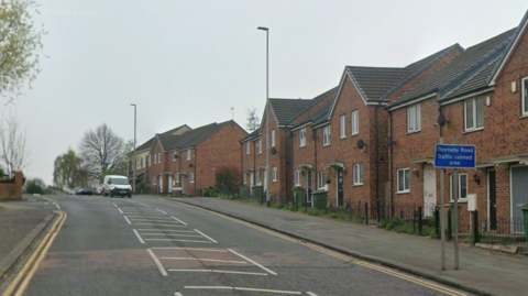 Thornaby Road is a residential street in Thornaby. It is a single-carriageway with one van travelling down it. There is a blue road sign reading 'Thornaby Road Traffic calmed area'. There are several terraced houses on the right side of the road.