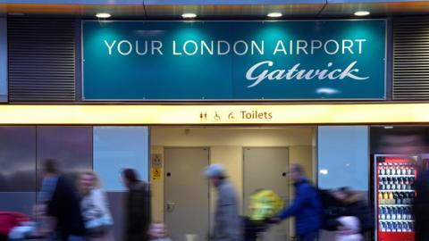 Passengers walk past a sign welcoming them to Gatwick Airport