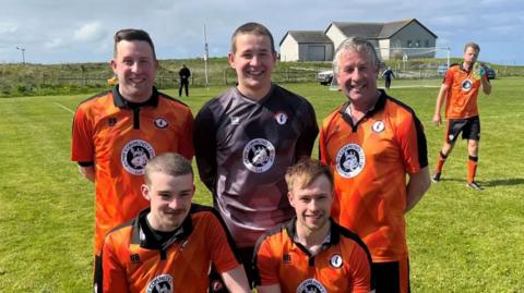A group of five footballers in orange strips and one in a goalkeeper's top