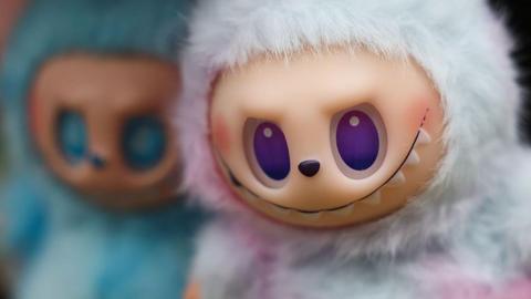 Two Labubu dolls in close focus. The one on the left is turquoise coloured and the one on the right has white and pink highlights. It has a big grin and purple eyes