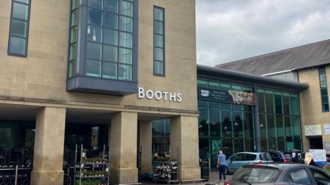 A supermarket with brick walls and large glass windows. There are cars parked outside