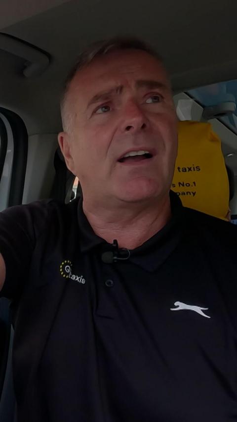 Man with grey hair and black top, sitting in the driver seat of a taxi
