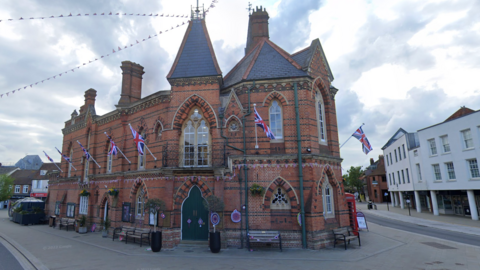 Wokingham Town Hall, an ornate building with red brick and arch windows, the building is decorated with Union Jack flags lined all around the exterior of the building