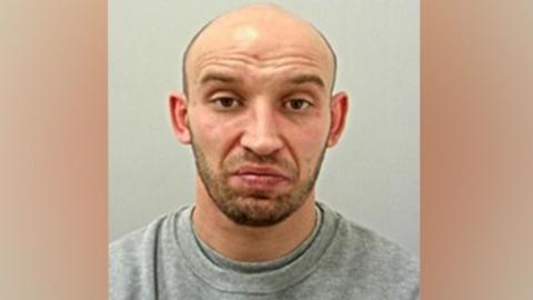 Slawomir Klimek's custody mugshot. A bald manwith brown eyes and dark stubble, he is wearing a grey sweatshirt.