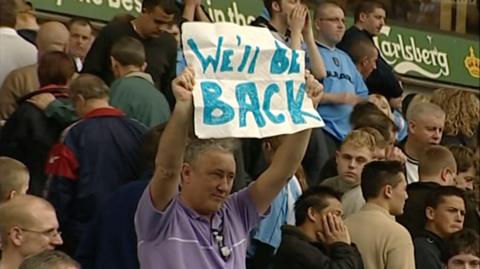 Coventry City fan John Mullaney holds a banner which writes "We'll be back" following the club's relegation from the Premier League.