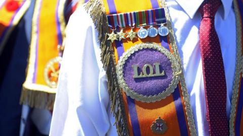 Image shows the torso of a man wearing an Orange Order Sash