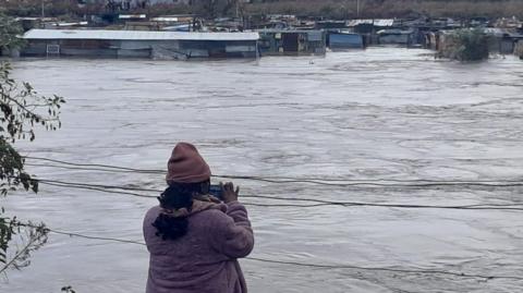 A woman takes pictures in front of a flooded body of water in South Africa's Eastern Cape province