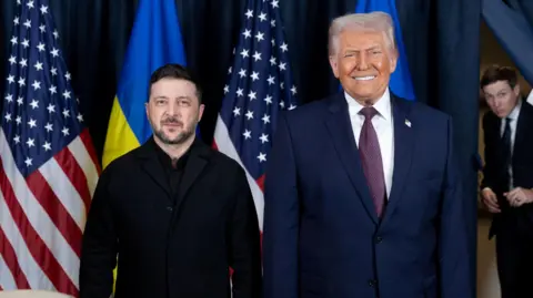 Volodymyr Zelensky (L) poses next to Donald Trump (R) for an official photo. Behind them are four flags, two Ukrainian and two American